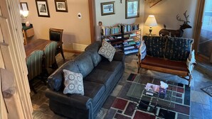 A living room with a dark leather sofa, a patterned armchair, a bookshelf, and a deer statue. - Deer Valley-100yds~1min walk. Closest Powder Run Penthouse. Deck Hot Tub w'Views (Park City)