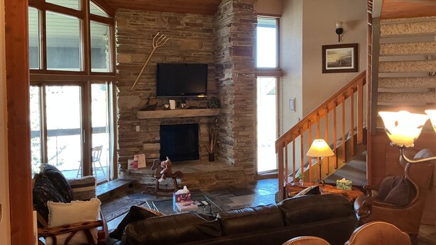 A cozy living room with a stone fireplace, a television, and a staircase. - Deer Valley-100yds~1min walk. Closest Powder Run Penthouse. Deck Hot Tub w'Views (Park City)