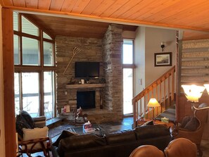 A cozy living room with a stone fireplace, a television, and a staircase.