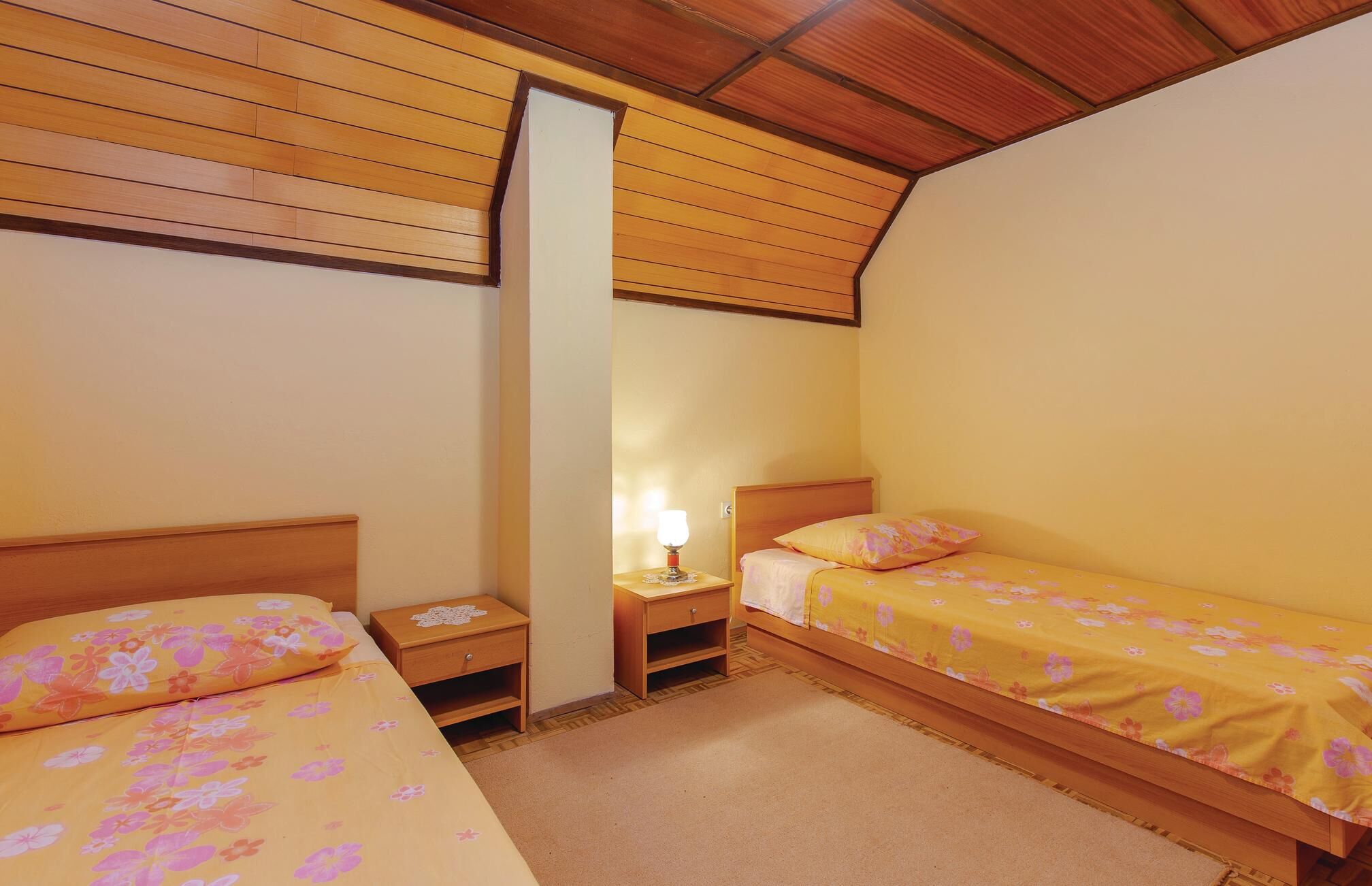 A small, cozy bedroom with two single beds, a nightstand with a lamp, and a wooden ceiling.