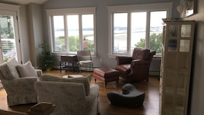 A spacious living room with large windows, a fireplace, and a view of the outdoors. - Oasis by the sea in Nahant  (Nahant)