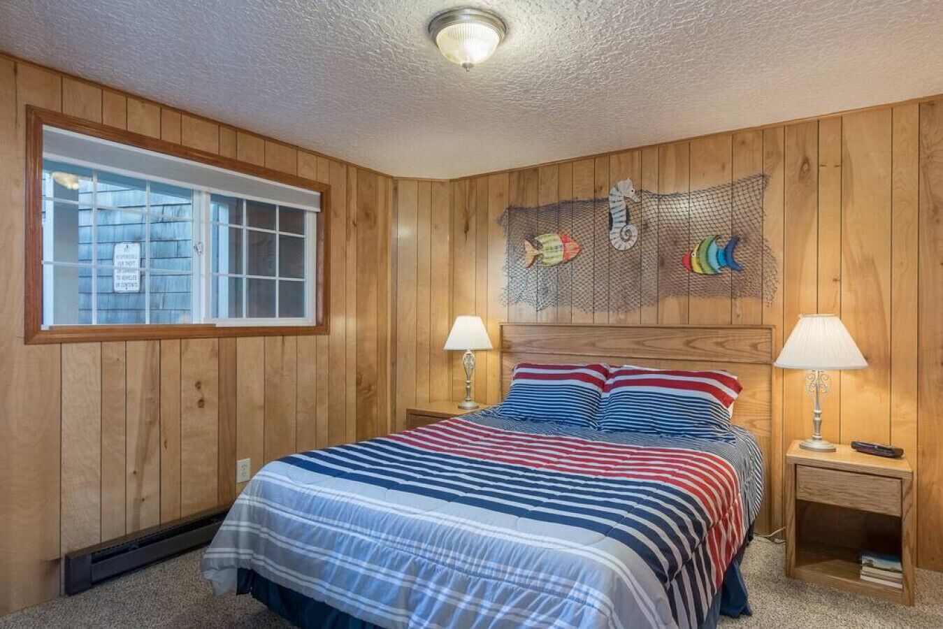 Un dormitorio con paneles de madera, una cama, dos lámparas de noche y un ventanal.