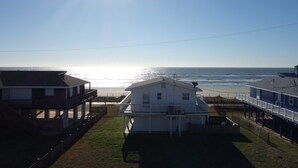 Ein Küstenhaus mit einem Balkon mit Blick auf den Strand, ein klarer Himmel und ein Sonnenuntergang über dem Meer.