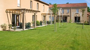 A building with a covered patio area, outdoor seating, and a well-maintained lawn. - Maison Près des Commerces (Bergerac)