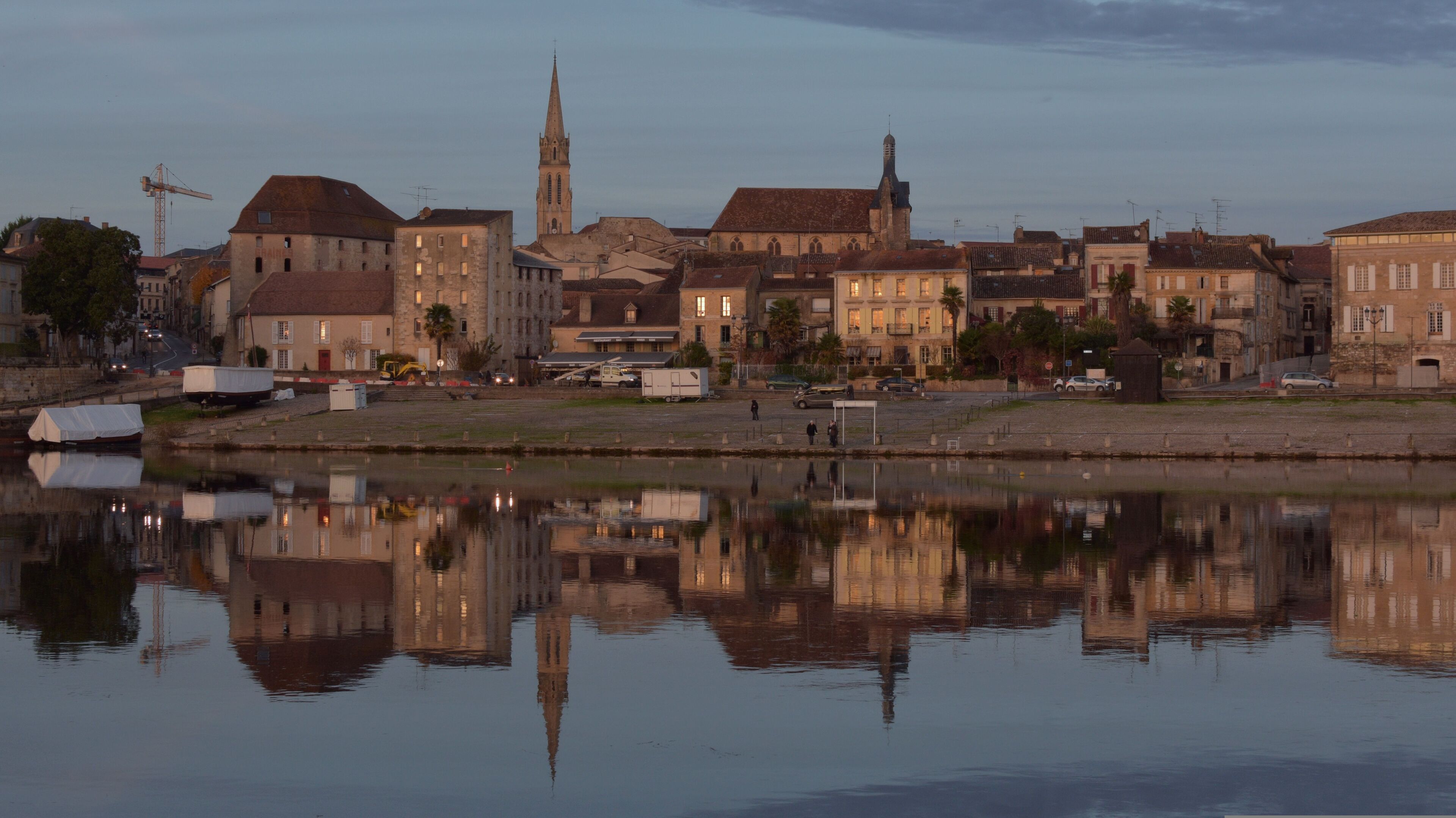Eine Flusslandschaft mit historischen Gebäuden, einem markanten Kirchturm und einer ruhigen Wasseroberfläche, die die Architektur spiegelt.
