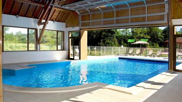 An indoor swimming pool with clear blue water, surrounded by tiled flooring and large windows. - Maison Près des Commerces (Bergerac)
