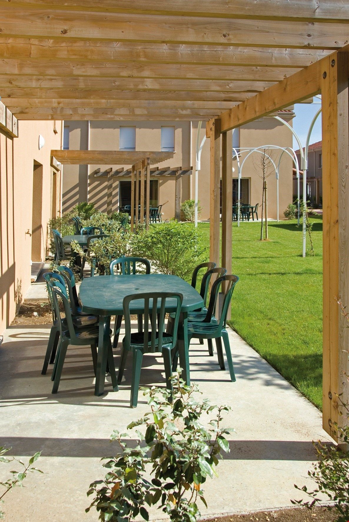 Une terrasse extérieure dotée d’une pergola en bois, d’une table ronde et de chaises vertes.