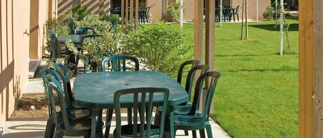 Une terrasse extérieure dotée d’une pergola en bois, d’une table ronde et de chaises vertes.
