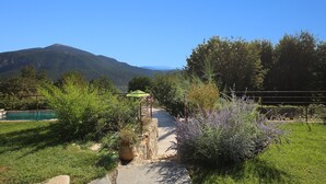 A pathway leading to a rustic wooden structure with a green roof, surrounded by lush greenery and a mountain in the background. - Provencal villa located in serene setting with panoramic views, sleeps 12 (Le Bar-sur-Loup)