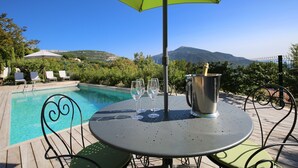 A poolside table with a green umbrella, two empty wine glasses, and a champagne bucket. - Provencal villa located in serene setting with panoramic views, sleeps 12 (Le Bar-sur-Loup)