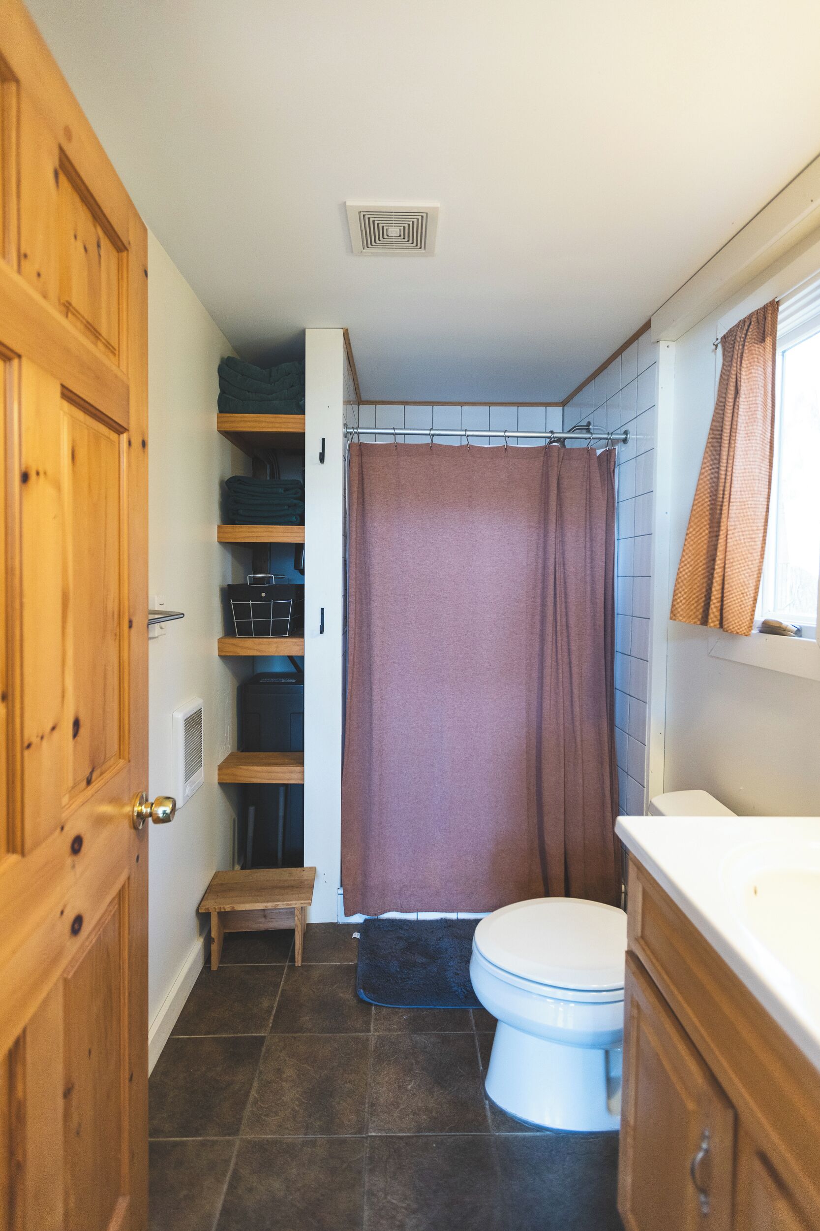 A compact bathroom with a white toilet, wooden cabinets, a shower curtain, and a small bench.