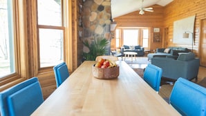 A dining area with a wooden table, blue chairs, and a fruit bowl. There is a stone wall and a ceiling fan. - Group Getaway on a Private Peninsula (Grand Rapids)
