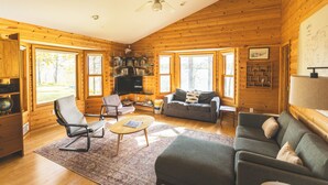 A log cabin interior with a living room, sofa, armchairs, a coffee table, and a bookshelf. - Group Getaway on a Private Peninsula (Grand Rapids)