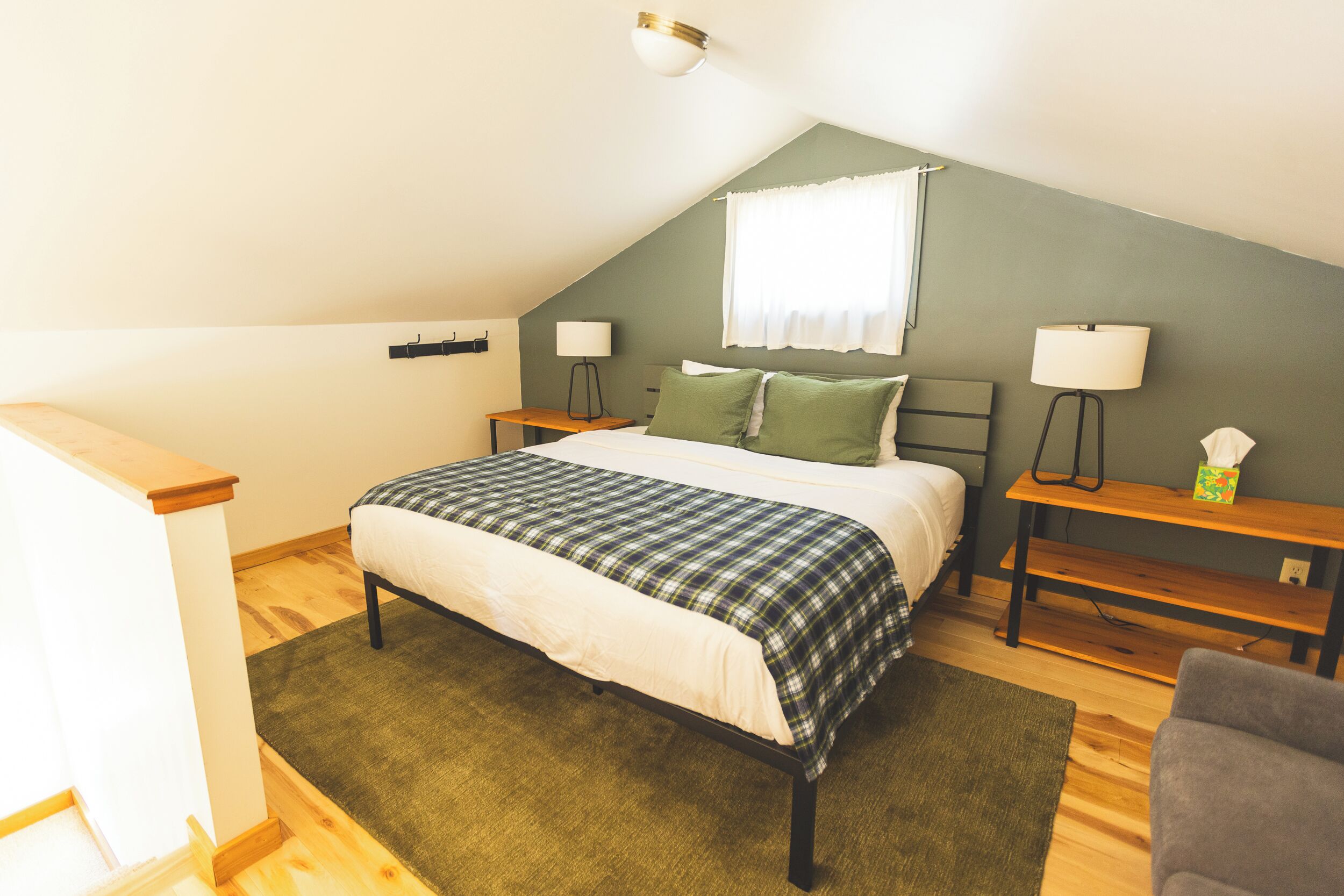 Une chambre à coucher avec un lit, deux tables de chevet, une lampe, une fenêtre avec des rideaux et un plancher en bois.