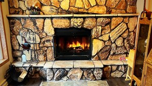 A stone fireplace with a fire, surrounded by a stone wall and a wooden floor.