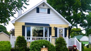 A two-story house with a white exterior and black shutters, a front porch with a white railing, and a sign indicating a pet-friendly establishment.