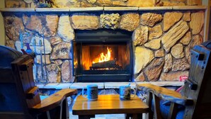 A stone fireplace with a fire, flanked by wooden furniture and a stone wall with decorative elements.