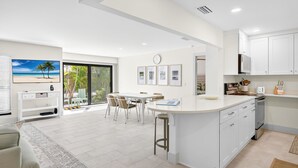 A modern kitchen with white cabinets, a central island, and a dining area with a view of the beach.
