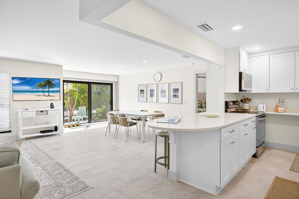 A modern kitchen with white cabinets, a central island, and a dining area with a view of the beach.