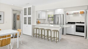 A modern kitchen with white cabinetry, a central island with stools, a refrigerator, and a stove.