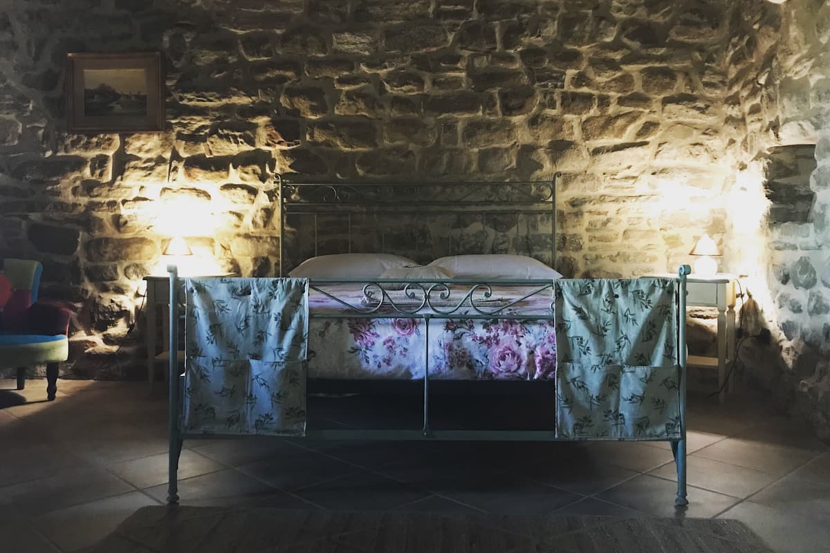 Une chambre avec un mur en pierre, un cadre de lit en métal, une couvre-lit à motifs floraux et deux lampes de chevet.