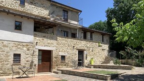 A stone building with a courtyard, a wooden door, and a small table with chairs. - Agriturismo la Palazzetta di Assisi (Assisi)