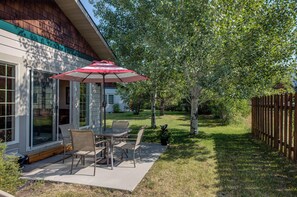 A patio with a table and chairs, a red umbrella, and a wooden fence in the background.
