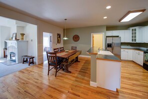 Uma cozinha ampla com piso de madeira, área de jantar com mesa e cadeiras de madeira, e armários brancos.