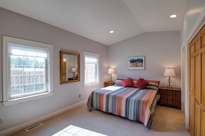 Quarto com cama, duas janelas, espelho, mesa de cabeceira, luminária, quadro na parede e armário.