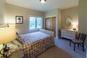A bedroom with a bed, dresser, chair, window, and a mirror.