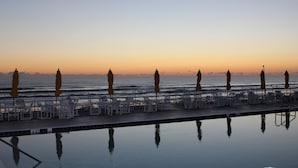 A poolside area with lounge chairs and umbrellas, overlooking the ocean at sunset. - Amazing Direct Oceanfront Condo. Steps to the Bch and Heated Pool. Gated complex (New Smyrna Beach)