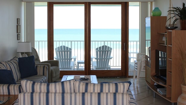 A living room with a view of the ocean, a sofa, chairs, a TV stand, and a lamp. - Amazing Direct Oceanfront Condo. Steps to the Bch and Heated Pool. Gated complex (New Smyrna Beach)