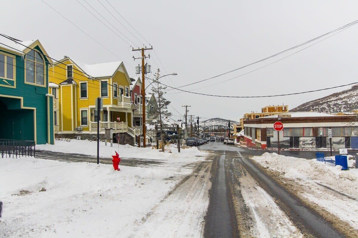 Une rue enneigée, bordée de maisons aux couleurs vives, et un panneau de signalisation.