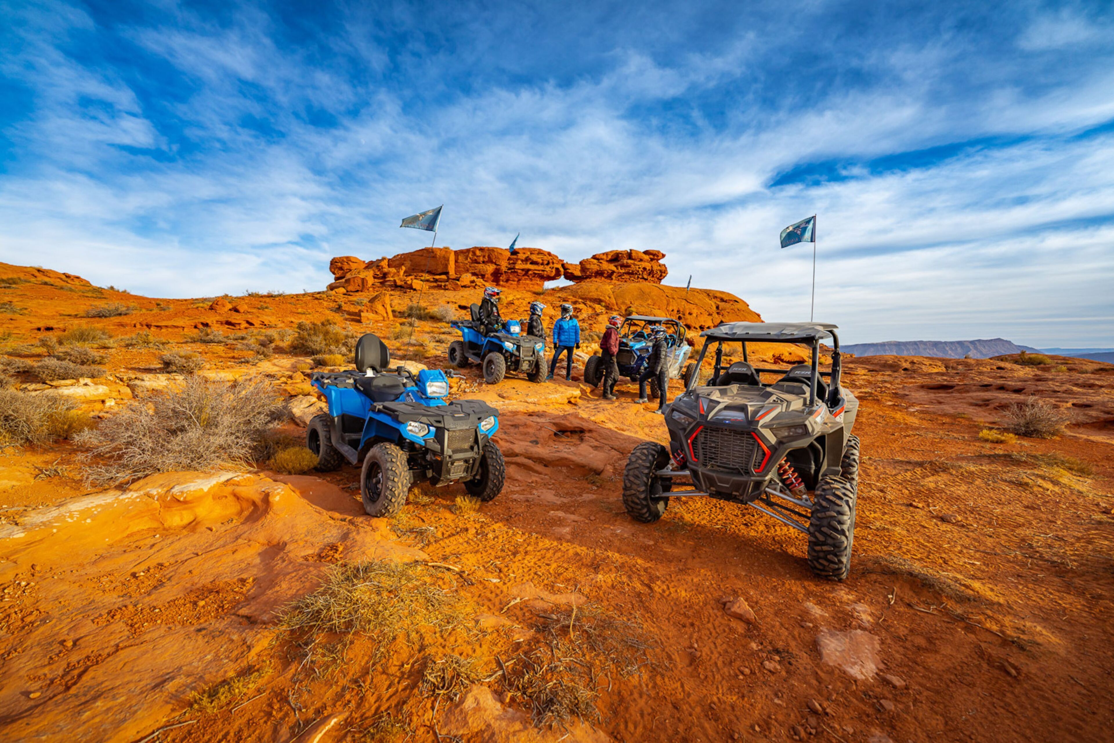 A group of off-road vehicles parked on a rocky terrain with a clear sky.
