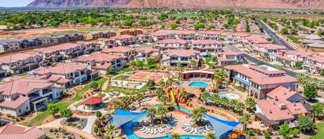 Un resort con varias construcciones, un área de piscina central y montañas al fondo.