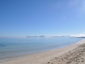 En strand med klare himmel, rolig vand og fjerne bjerge.