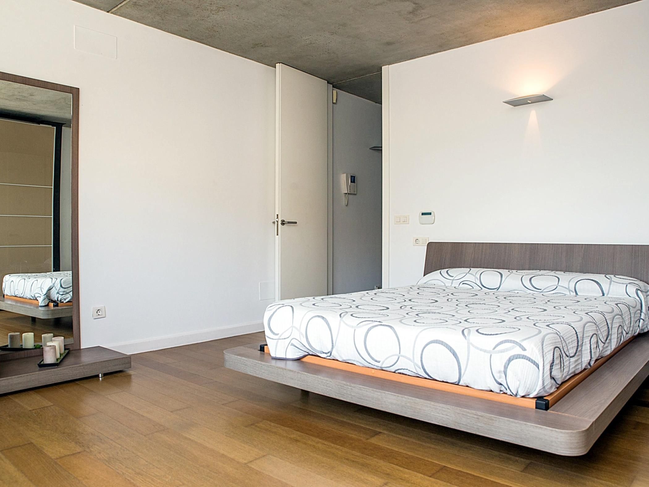 Een moderne slaapkamer met een bed, nachtkastje, spiegel en een deur.