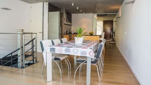 A modern dining area with a table set for six, a staircase, and a kitchen in the background.