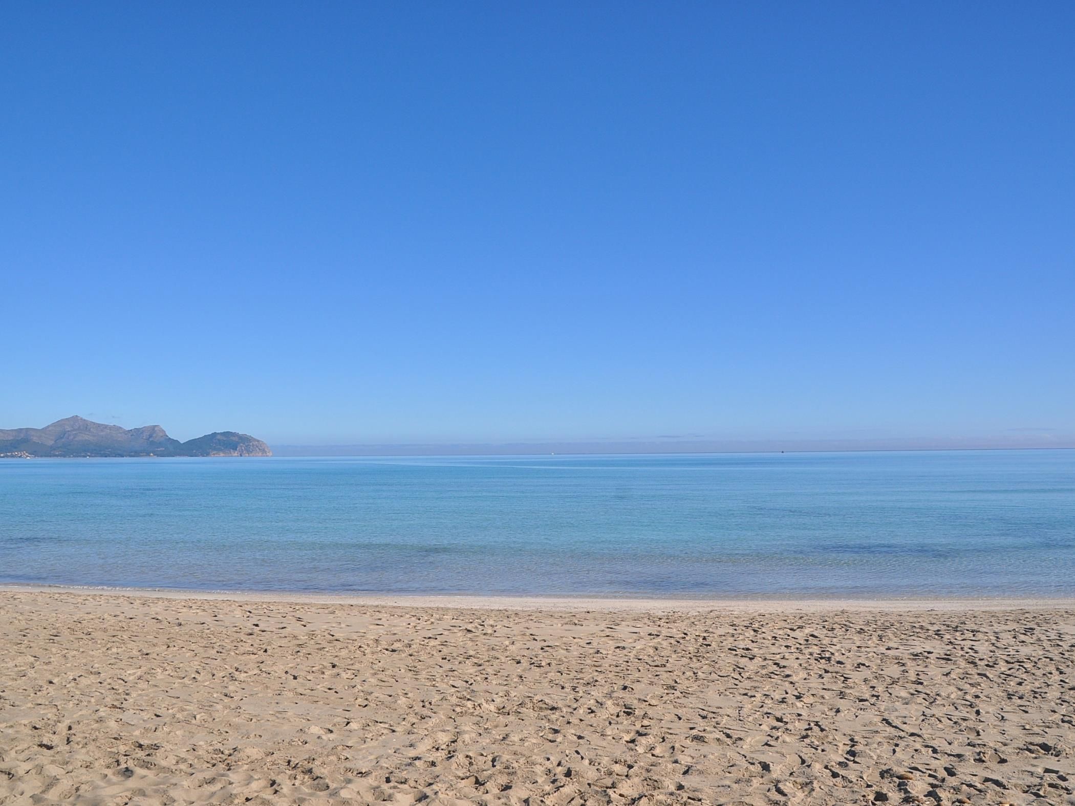 Een zandstrand met helderblauw water en op de achtergrond bergen.
