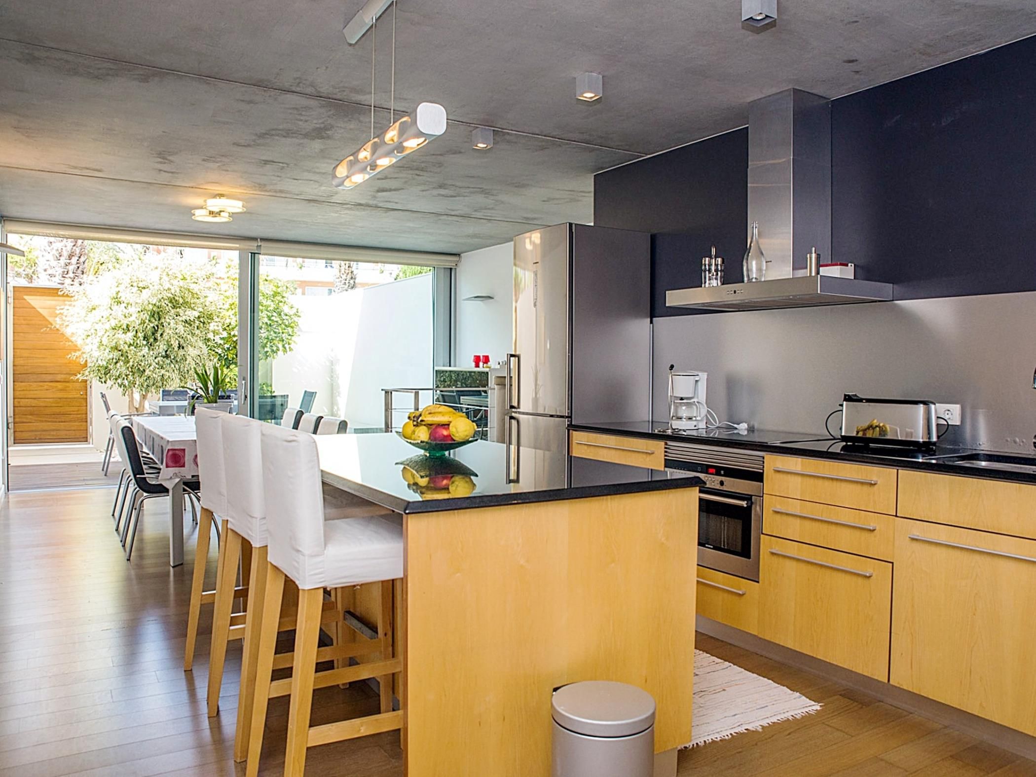 Een moderne keuken met een centraal eiland, roestvrijstalen apparatuur en een eethoek met een glazen deur naar een buitenruimte.