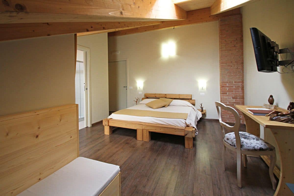 A bedroom with a wooden bed, a desk, and a chair. There is a television mounted on the wall.