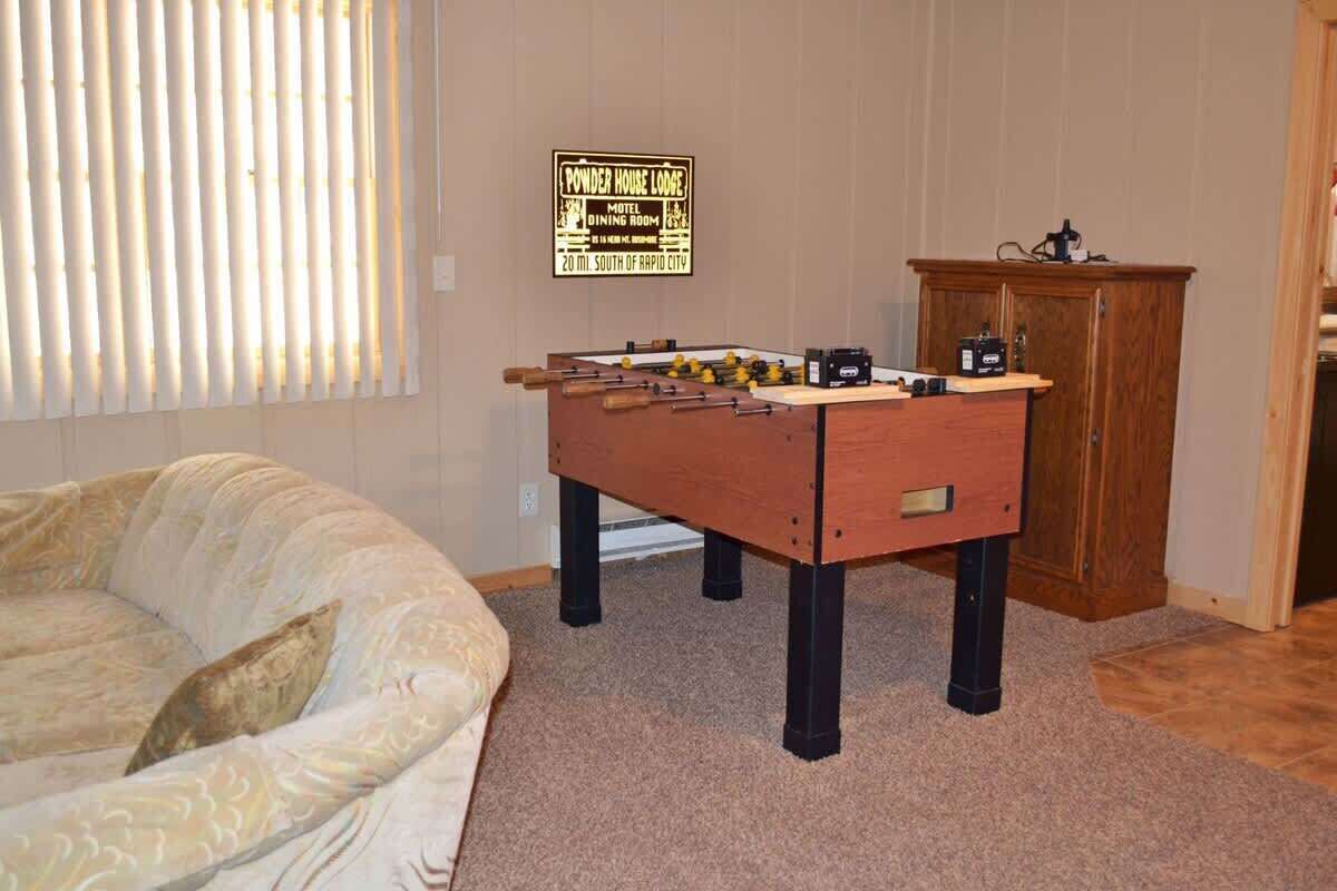 A room with a foosball table, a bed, and a wooden cabinet.
