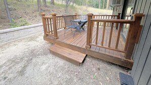 A wooden deck with a metal table and chairs, a stone wall, and a forested hillside in the background. - Keystone Crossing (Keystone)