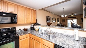 A kitchen with wooden cabinets, granite countertops, a black microwave, a stove, a sink, and a ceiling fan. - The Cove - Unit 1302 - FREE Attraction Ticket with EACH night Stay Including Dollywood (Pigeon Forge)