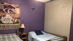 A room with two beds, a purple wall, a Kansas State University tapestry, and a WeVKSU sign. - Sportsman's Paradise (Stockton)