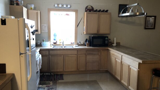A kitchen with wooden cabinets, a microwave, a sink, and a window with natural light. - Sportsman's Paradise (Stockton)