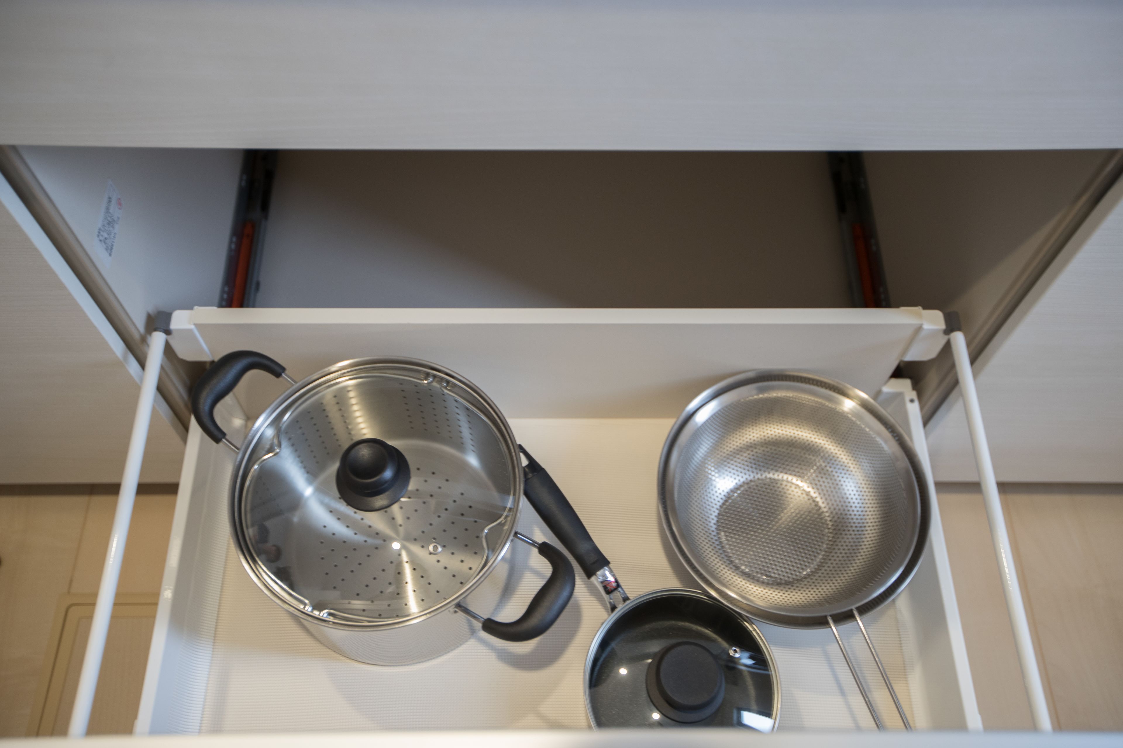A kitchen drawer with three stainless steel pots and pans.