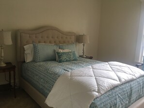 A bedroom with a tufted headboard, a patterned bedspread, and two bedside lamps.