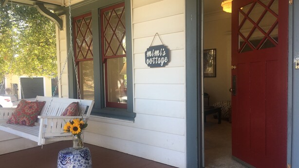 A porch with a white bench, a blue and white vase with sunflowers, and a sign reading "Mimi's Cottage." - Mimi's Downtown Cottage (Lodi)