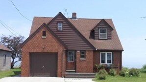 A two-story brick house with a brown roof, a garage, and a front yard with a sidewalk.